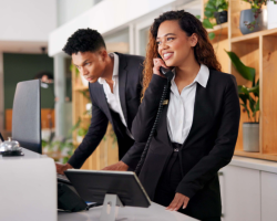 Eine Frau und ein Mann stehen an einer Rezeption, die Frau telefoniert und der Mann schaut auf den Computer